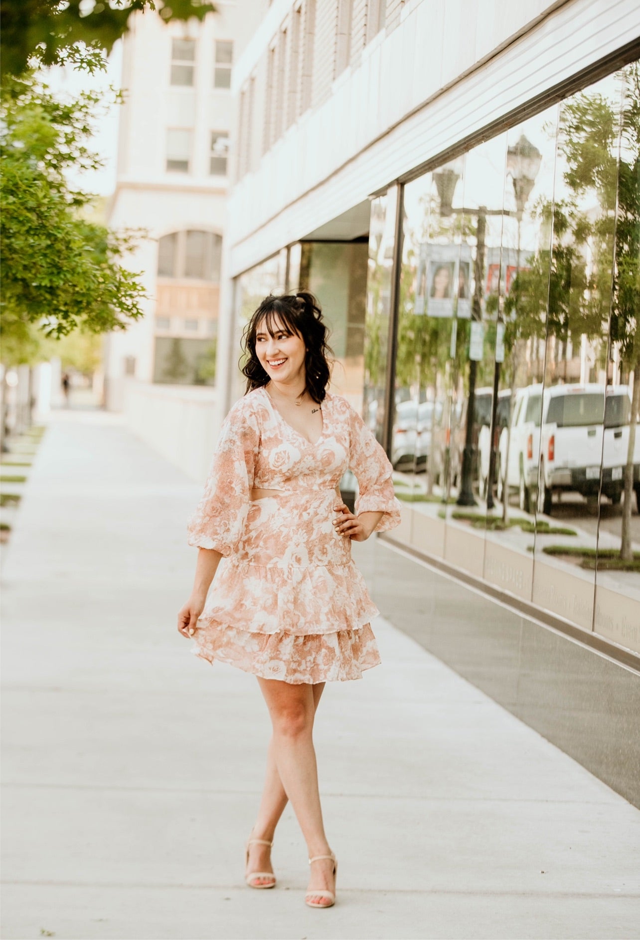 A flowy white dress adorned with soft, light burnt orange floral patterns, creating a fresh and vibrant look. It features stylish cut-outs on the sides for a modern touch, and a flattering V-neckline at the chest for added elegance. The dress falls right above the knee, offering a perfect balance of comfort and chic, ideal for casual outings or a daytime event.